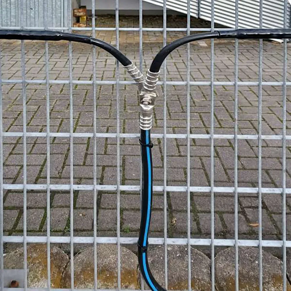 Three cables are joined together and wrapped with tape at a junction, running vertically against a metal fence with a brick pavement in the background.