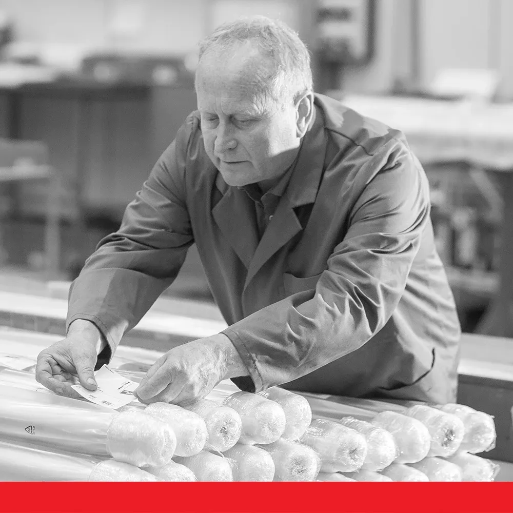 Worker in a workshop placing labels on wrapped cylindrical products.