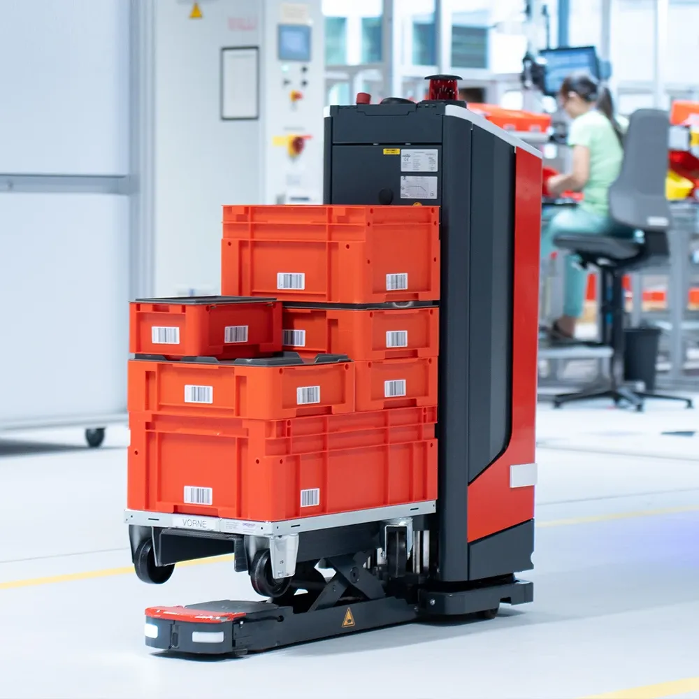 Autonomous mobile robot transporting stacked red plastic crates in a production facility.
