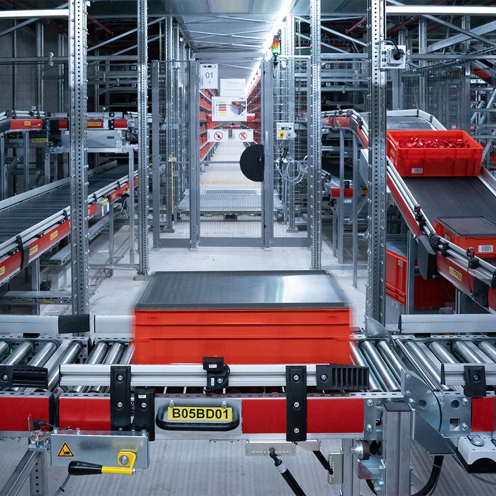 Automated warehouse system with red storage bins moving along conveyor belts inside a metal rack structure.