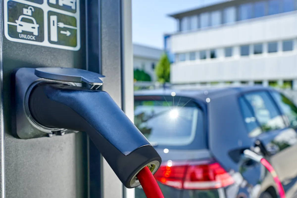 Electric vehicle charging station with a red charging cable connected to a dark gray car.
