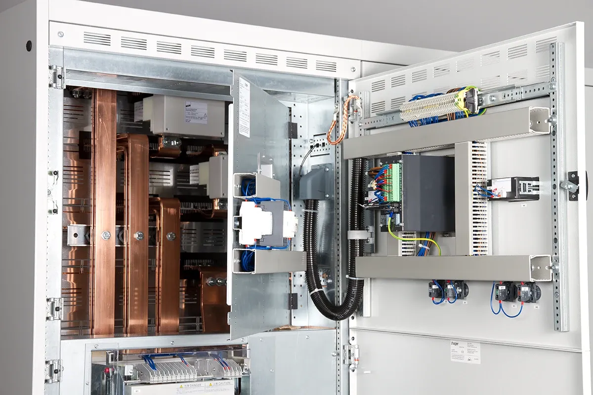 Open electrical cabinet with large copper busbars, wiring, terminals and control components mounted on the door and frame.