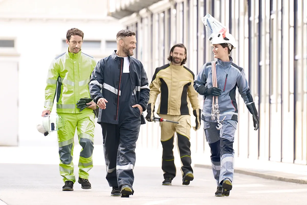 Four workers in protective clothing walking together outdoors, carrying safety gear and tools.